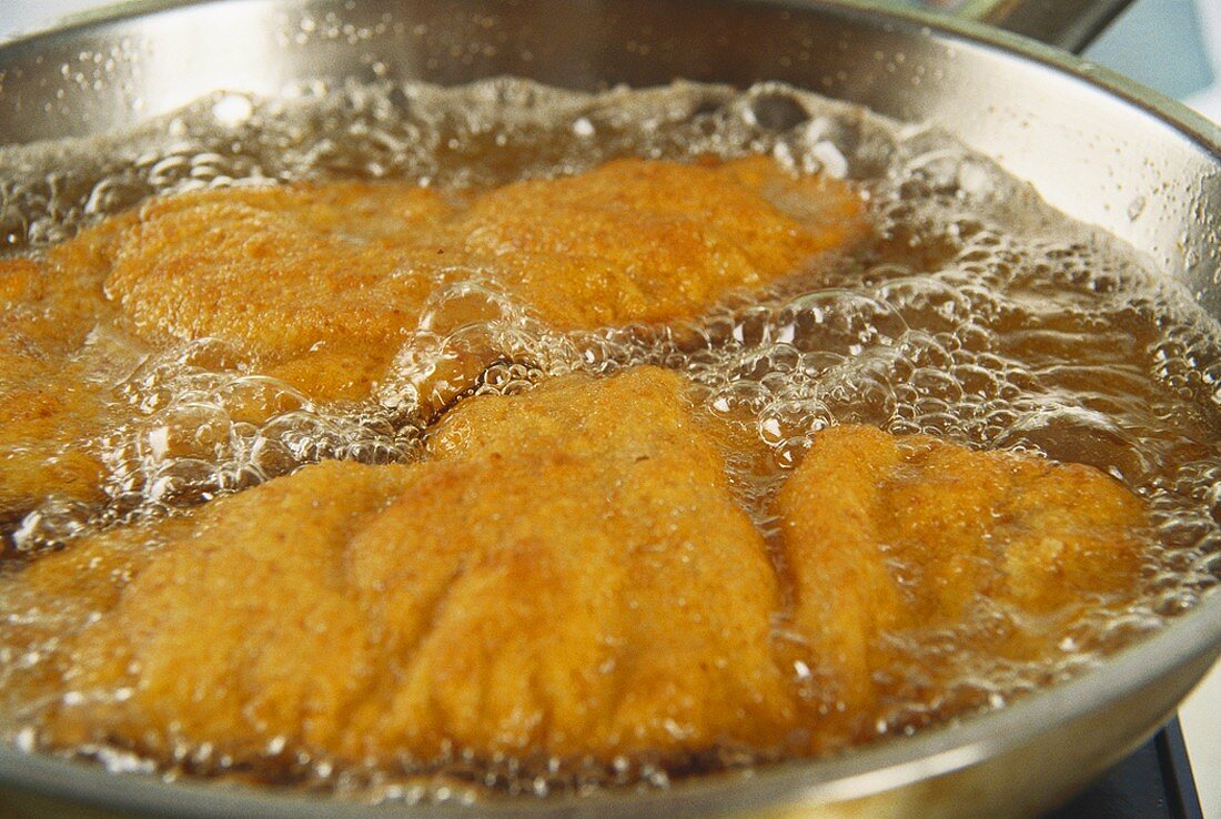 Two breaded escalopes being fried in a frying pan