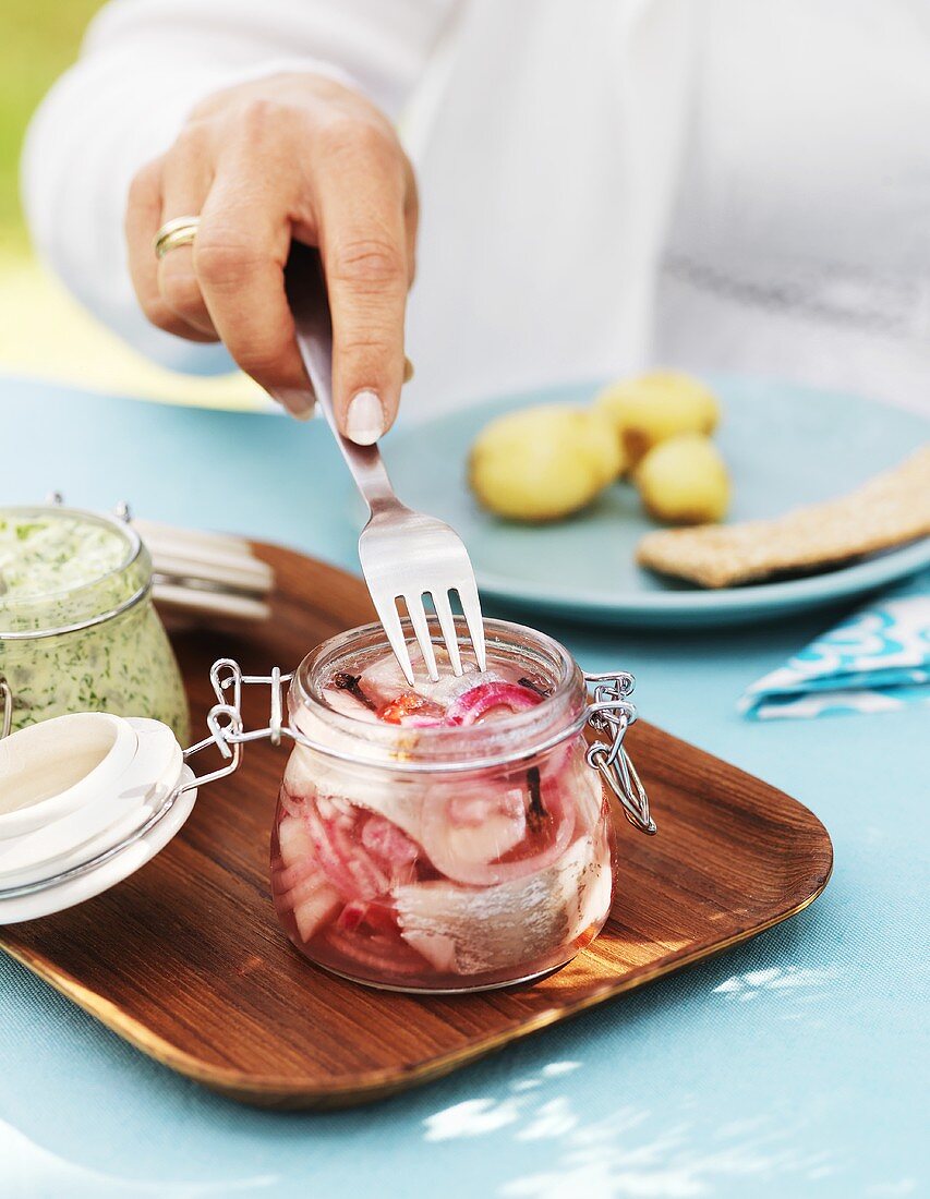 Woman spearing a pickled herring in a jar with a fork