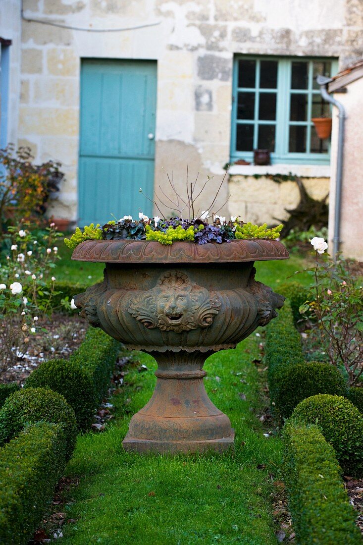 Flowers in stone vase in country garden (house in background)