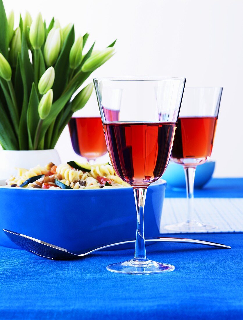 Nudelsalat in blauer Schale, Roseweingläser und Tulpen auf Tisch