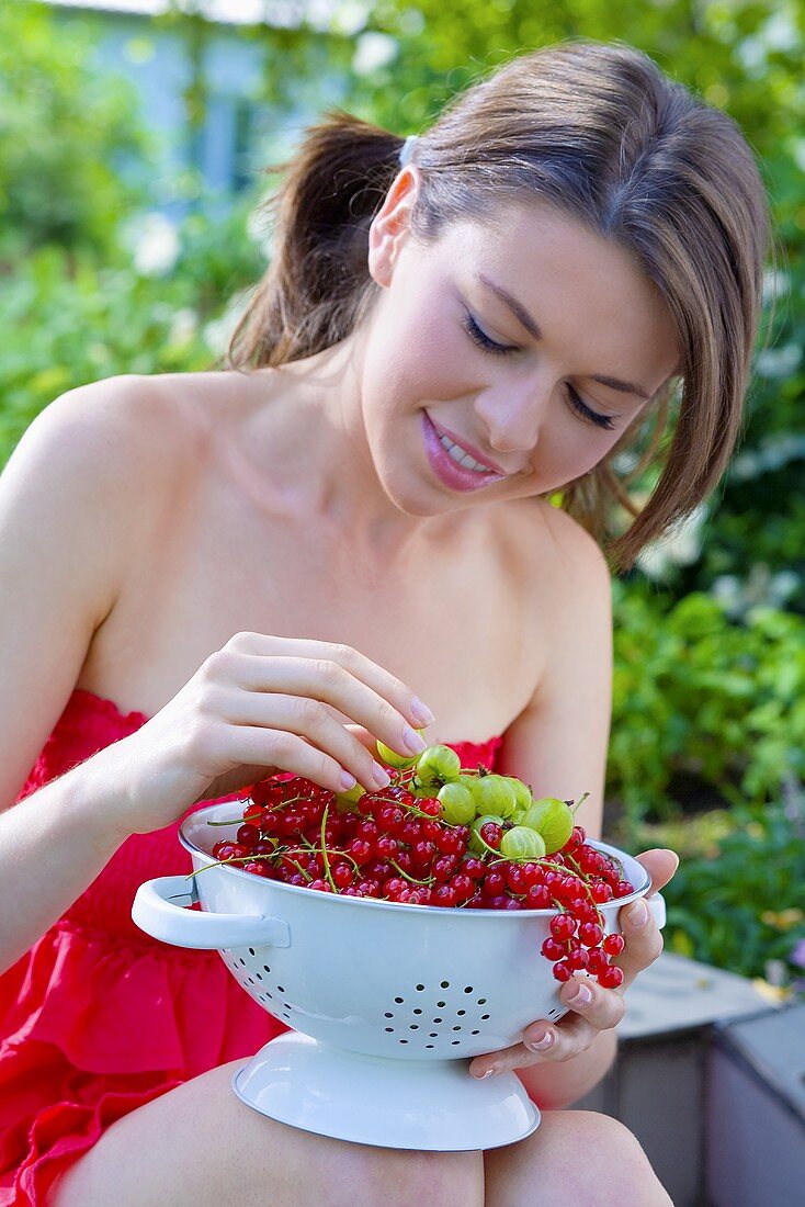 Junge Frau hält Metallsieb mit Johannisbeeren & Stachelbeeren