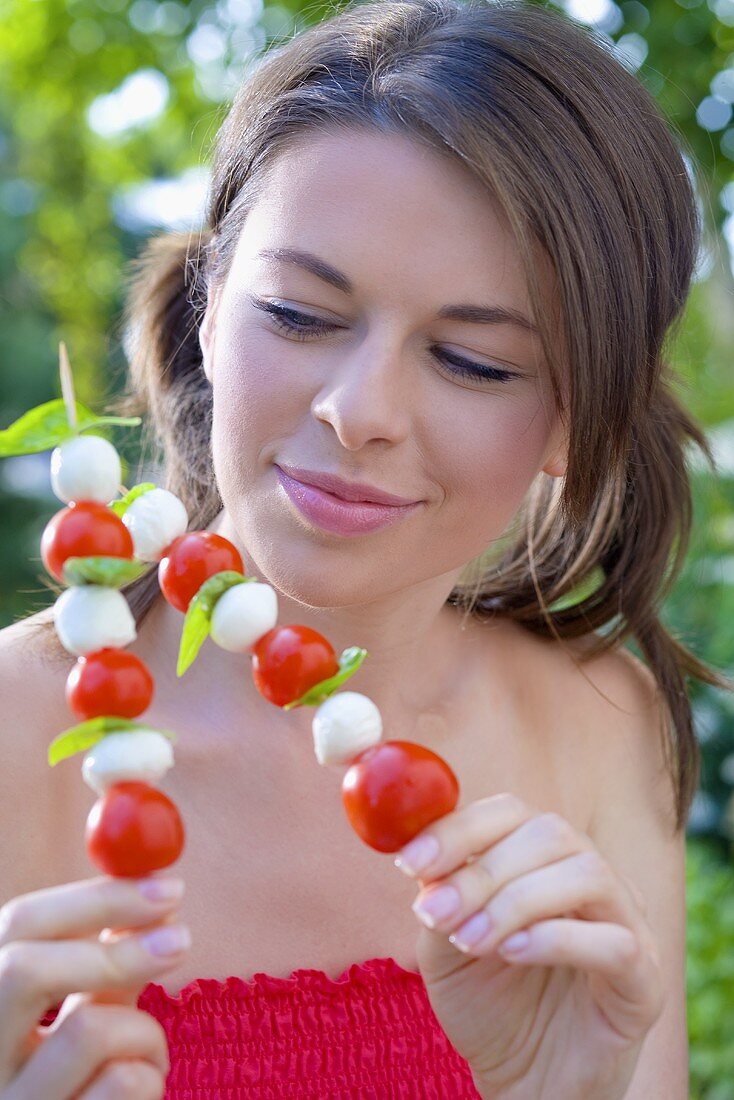 Young woman with tomato and mozzarella skewers