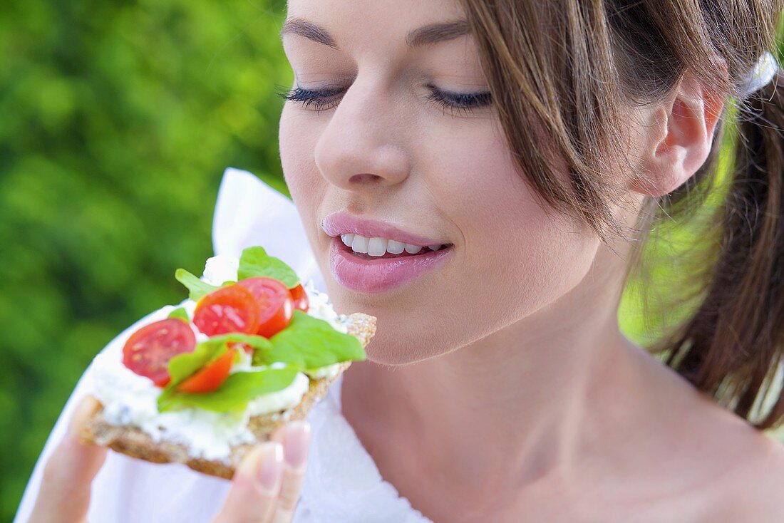 Junge Frau isst Knäckebrot mit Hüttenkäse, Tomaten und Basilikum