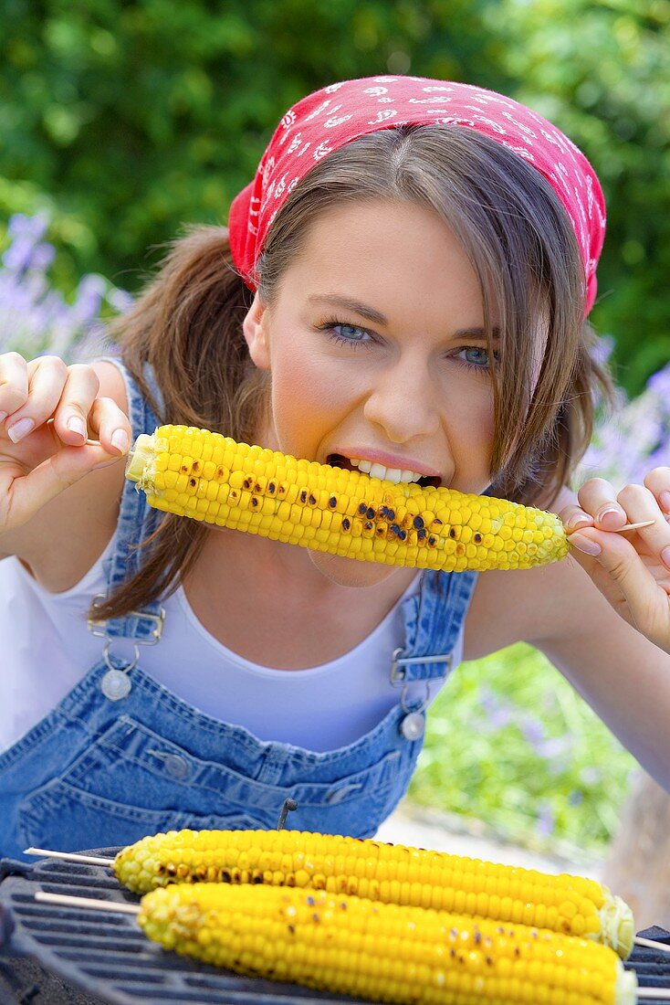 Junge Frau isst gegrillten Maiskolben
