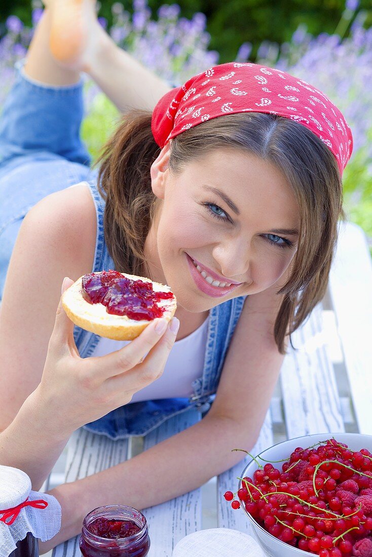 Young woman eating bread roll with jam