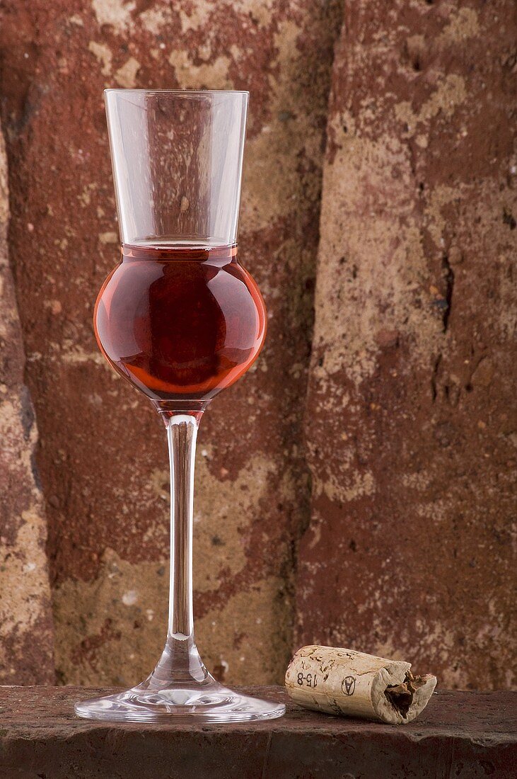 Liqueur in grappa glass on brick wall, cork beside it