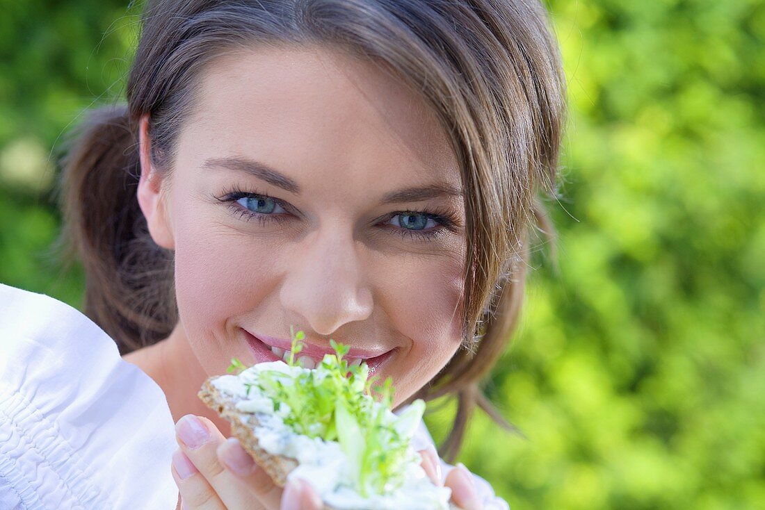 Young woman eating crispbread with cottage cheese & cucumber