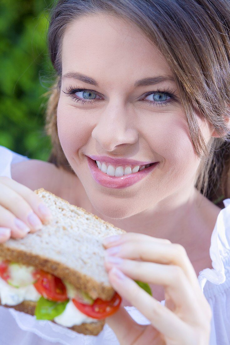 Junge Frau isst Sandwich mit Hüttenkäse, Tomaten & Basilikum
