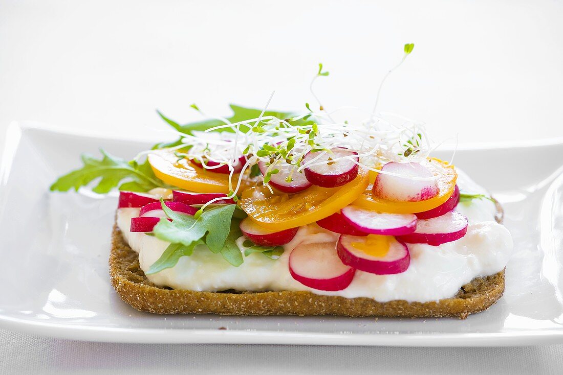 Brötchenhälfte mit Sauerrahm, Tomaten, Radieschen und Rucola