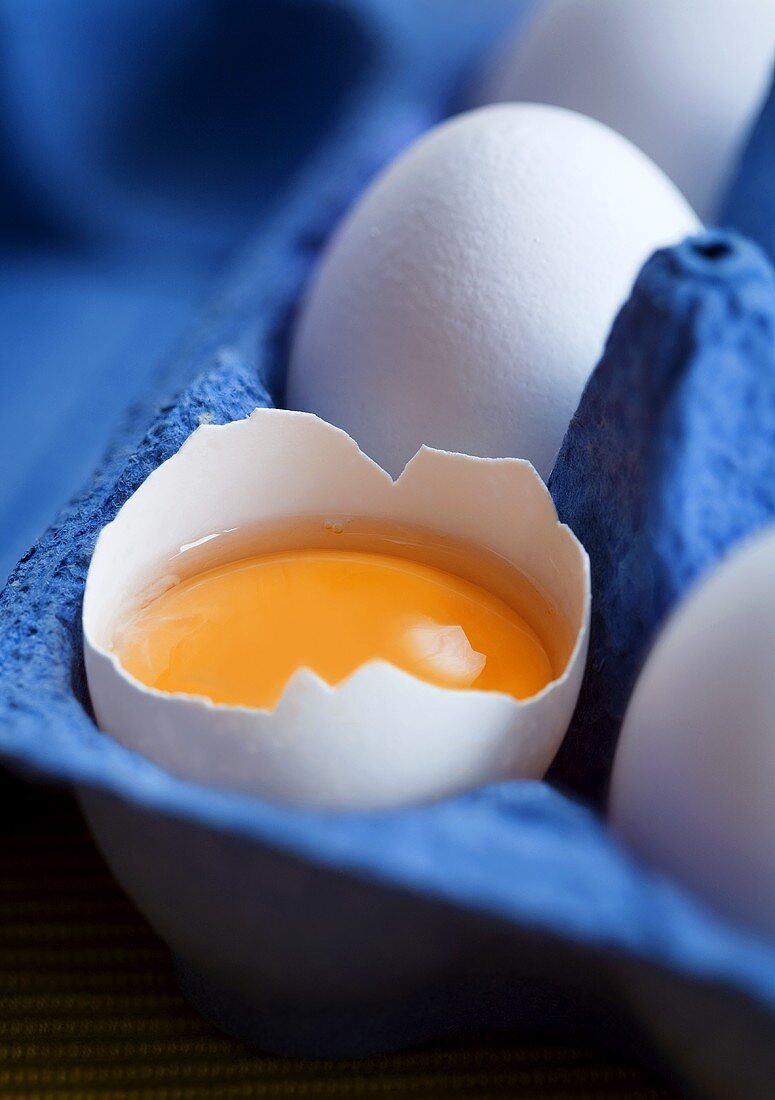 Egg, cracked open, in egg box (close-up)