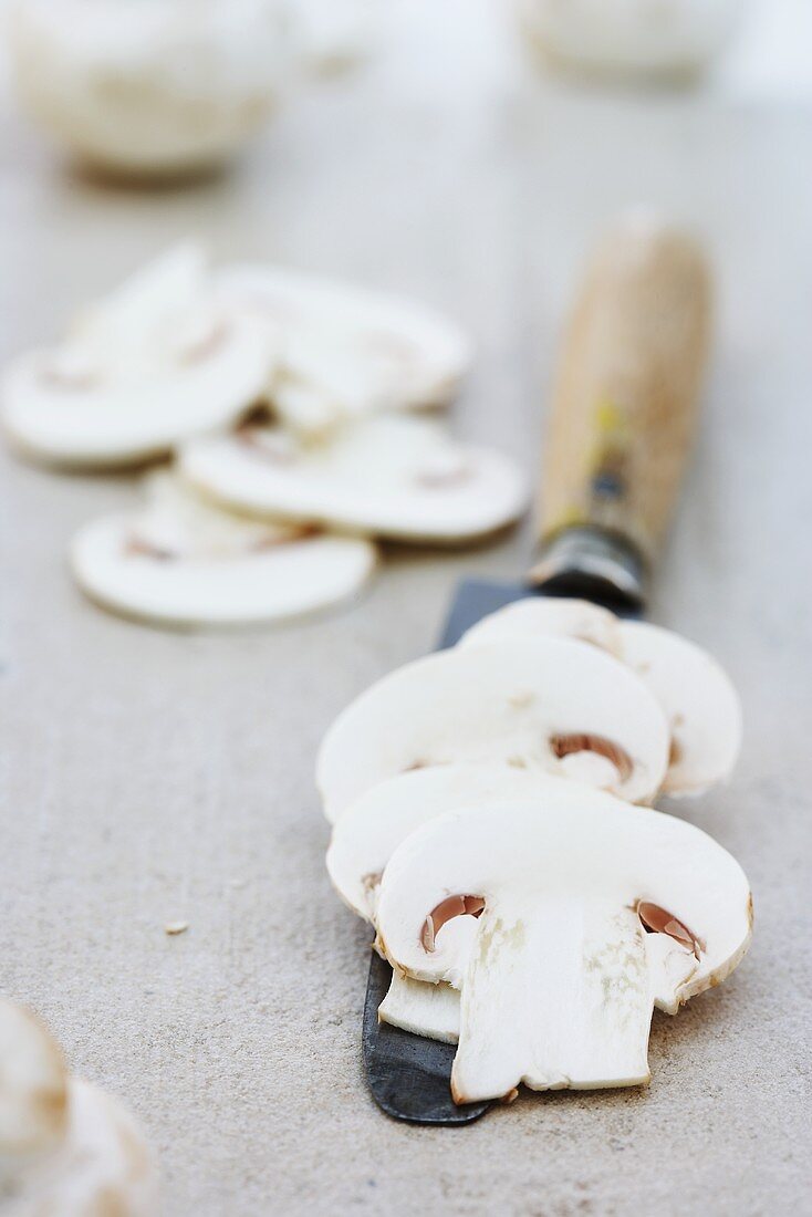 Sliced button mushrooms on and beside knife