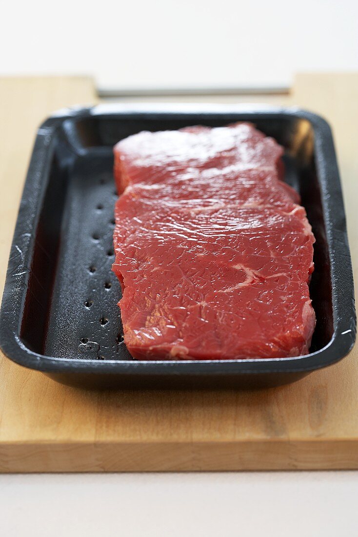 Beefsteak in polystyrene tray on chopping board
