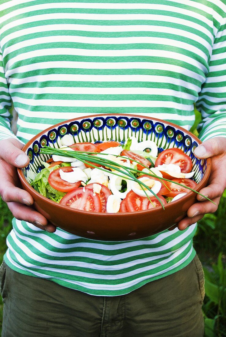 Person hält Salatschüssel mit Tomaten, Ei, Blattsalat und Schnittlauch