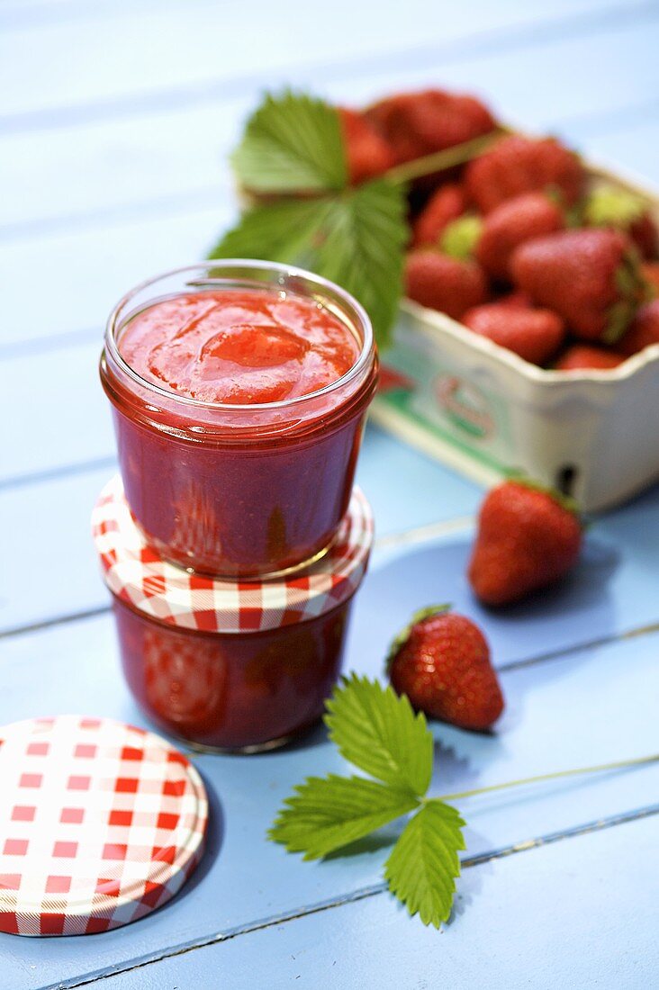 Two jars of strawberry jam and fresh strawberries