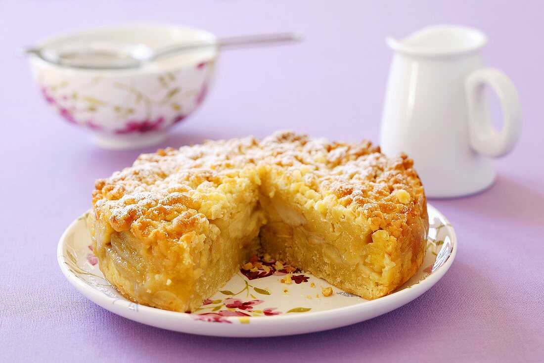 Apple crumble cake with icing sugar, cream jug