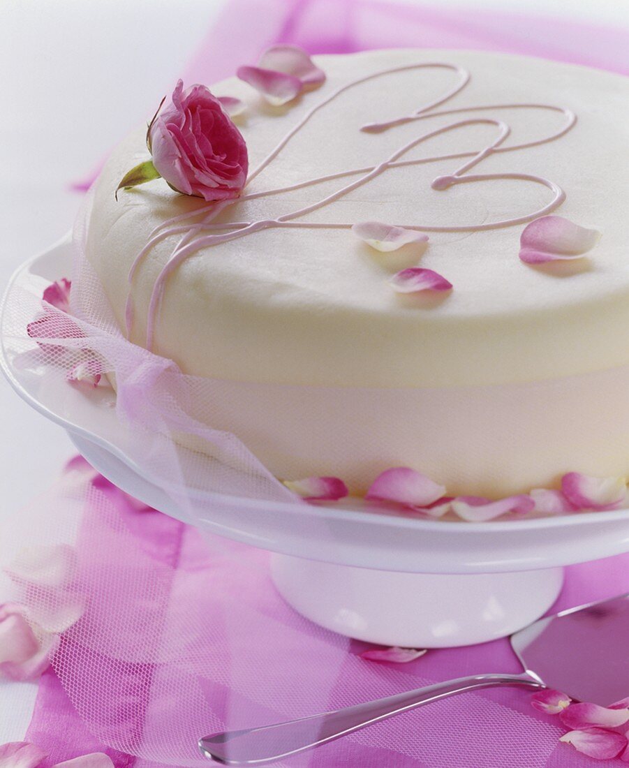 weiße Torte mit Rosenblättern, rosa Herzen und Schleife