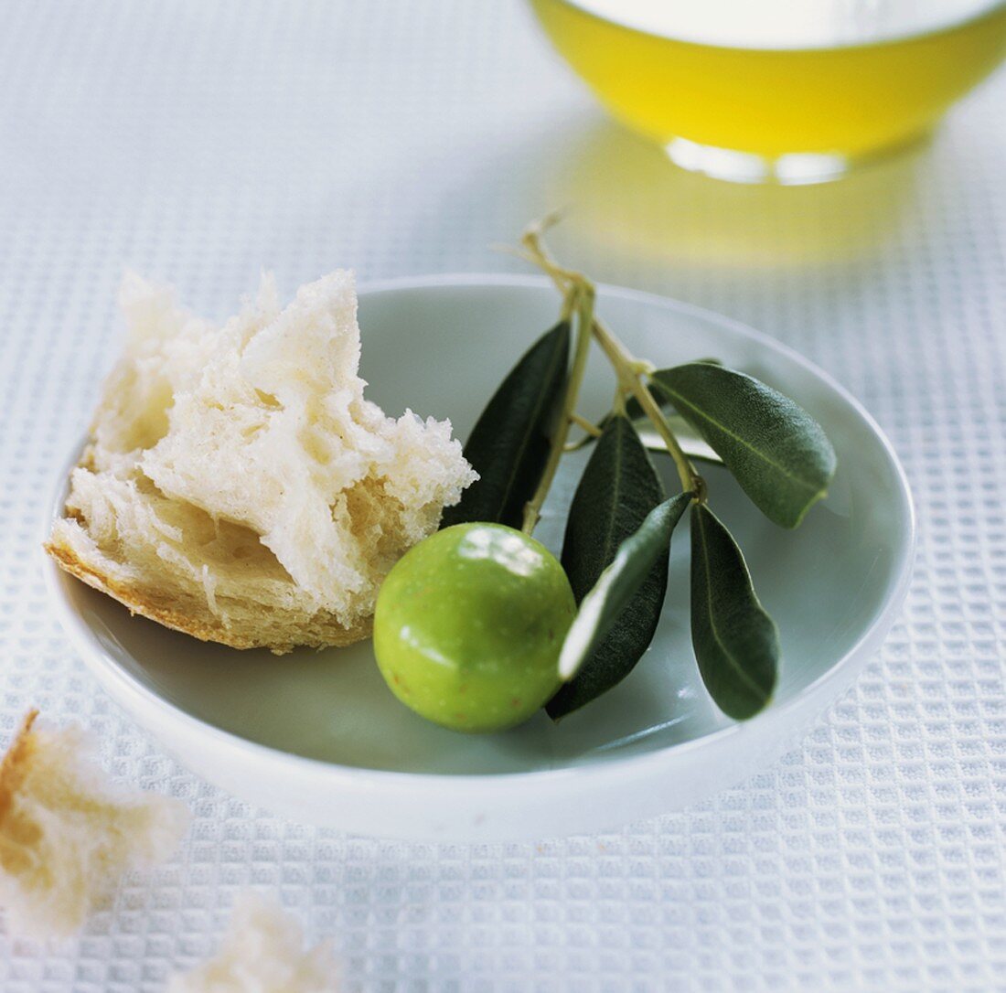 Grüne Olive, Olivenzweig, Weißbrot, im Hintergrund Olivenöl