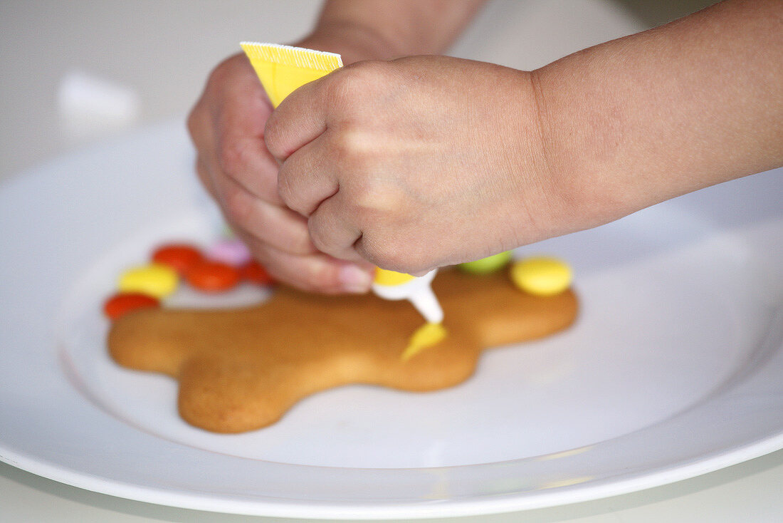 Child's hands decorating a gingerbread man with writing icing
