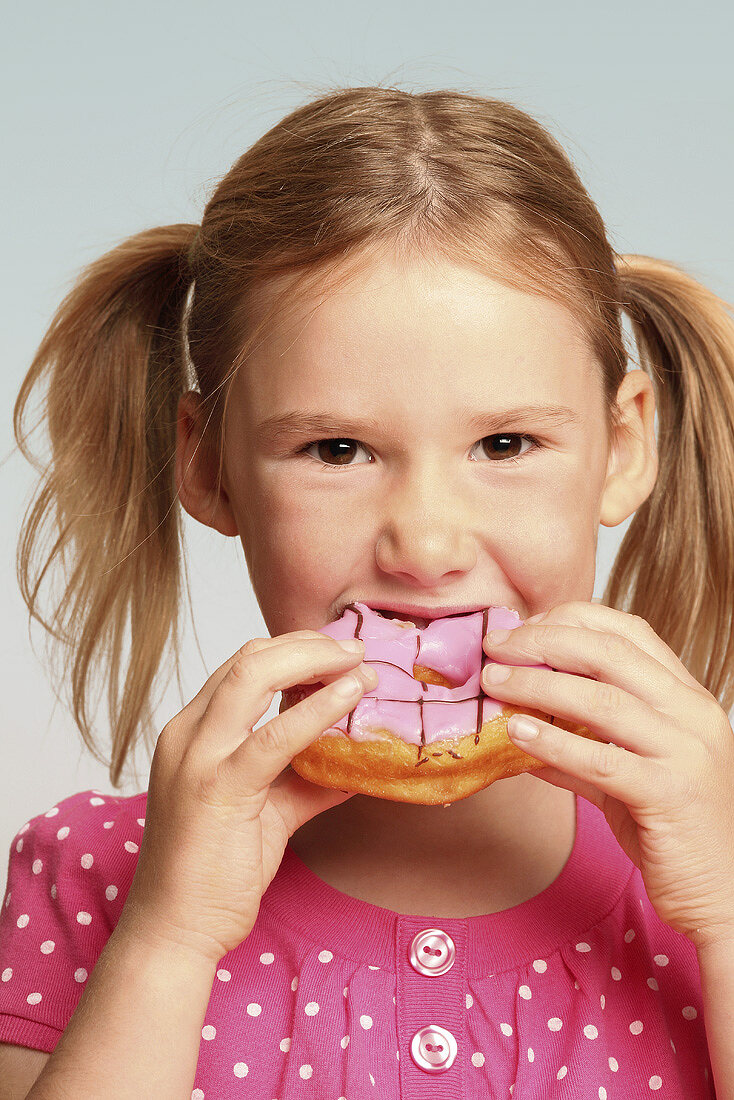 Mädchen isst Doughnut mit Zuckerglasur