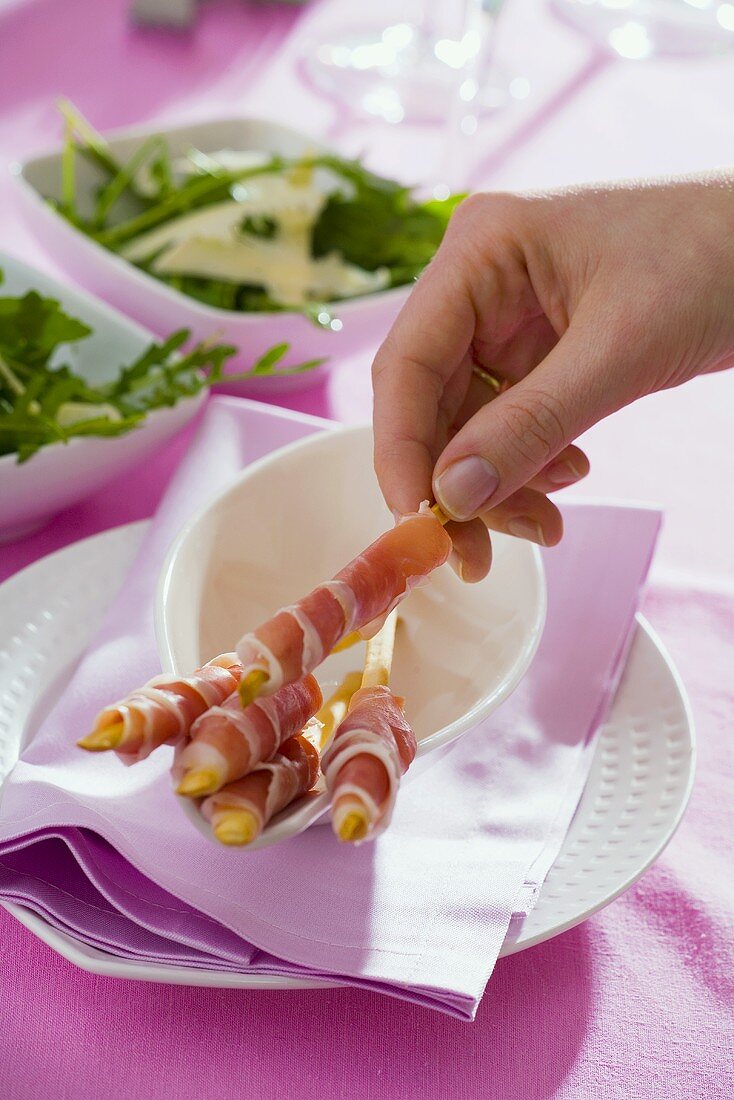 Hand holding grissini wrapped in Parma ham