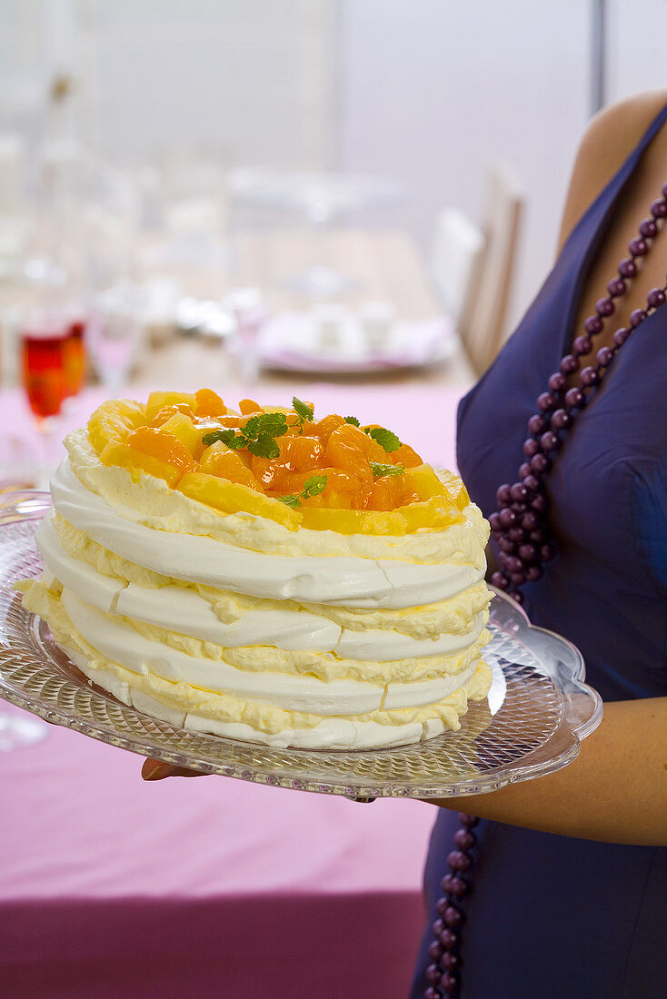 Young woman holding layered meringue cake with citrus fruit