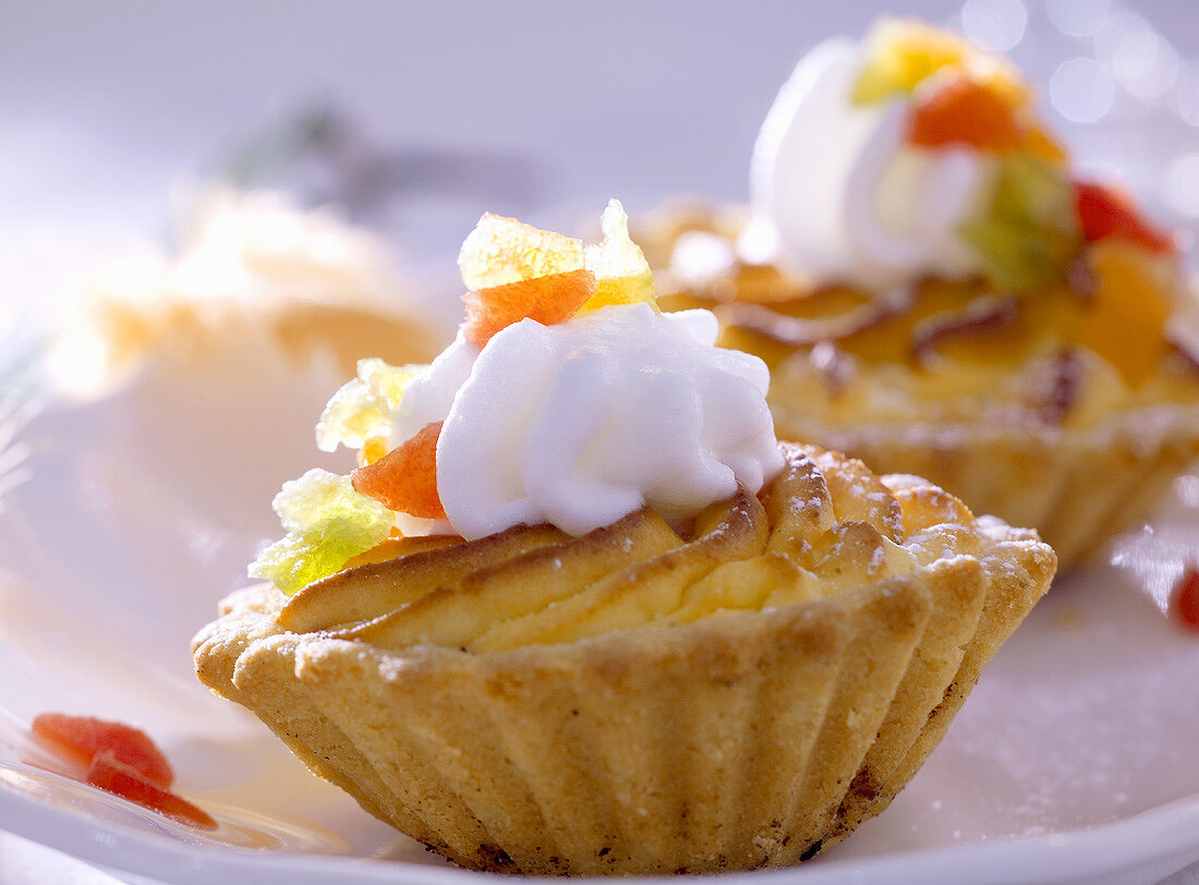 Cheese tarts topped with cream & candied fruit (close-up)