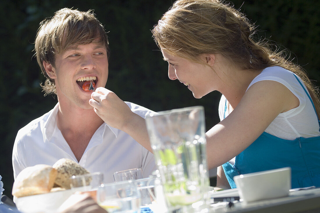 Young woman feeding a young man a tomato