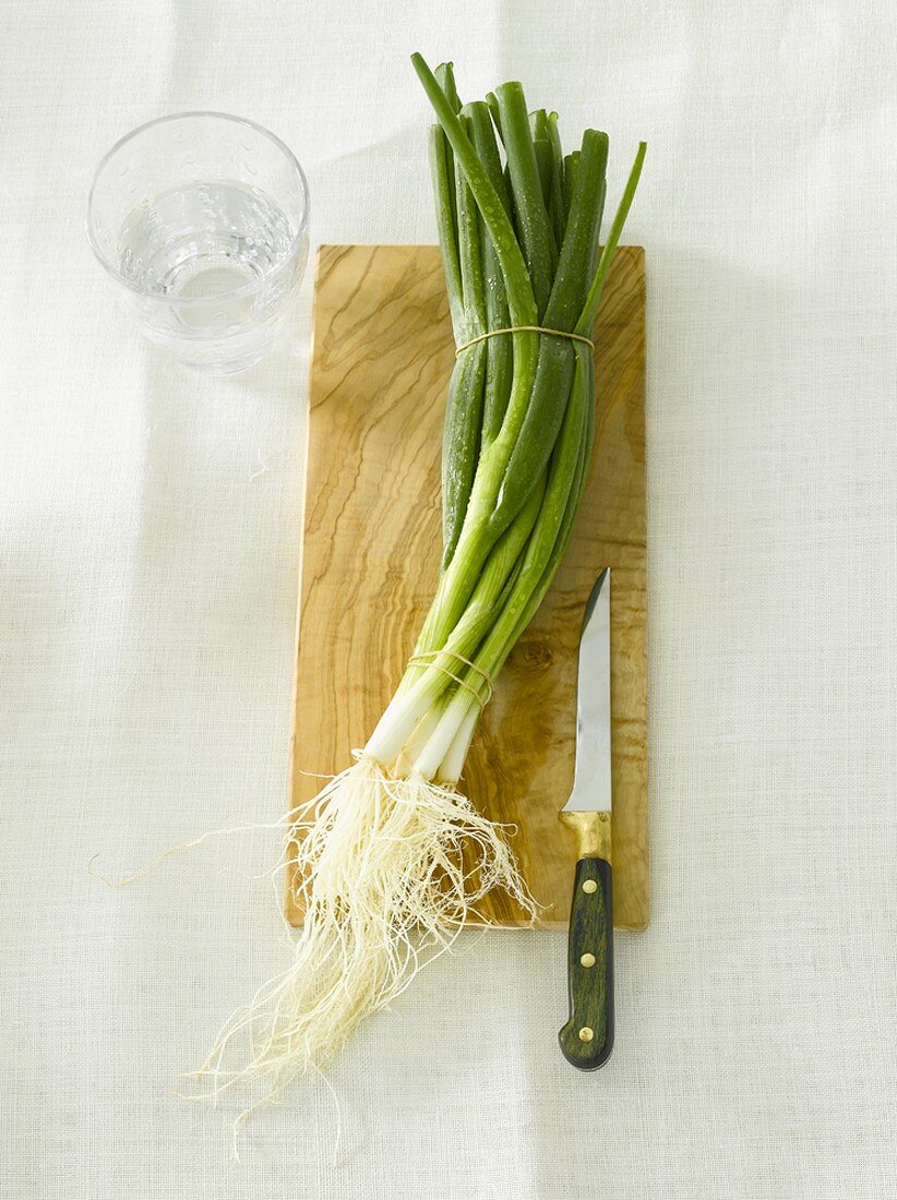 Spring onions on wooden board with knife, glass of water