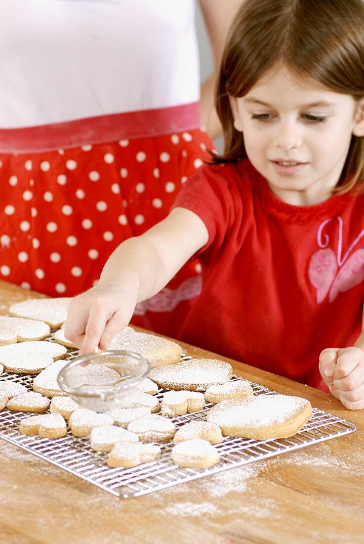Girl dusting biscuits with icing sugar