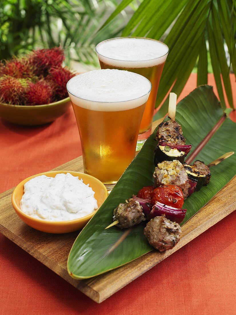 Grilled lamb kebabs on banana leaf, yoghurt dip and beer