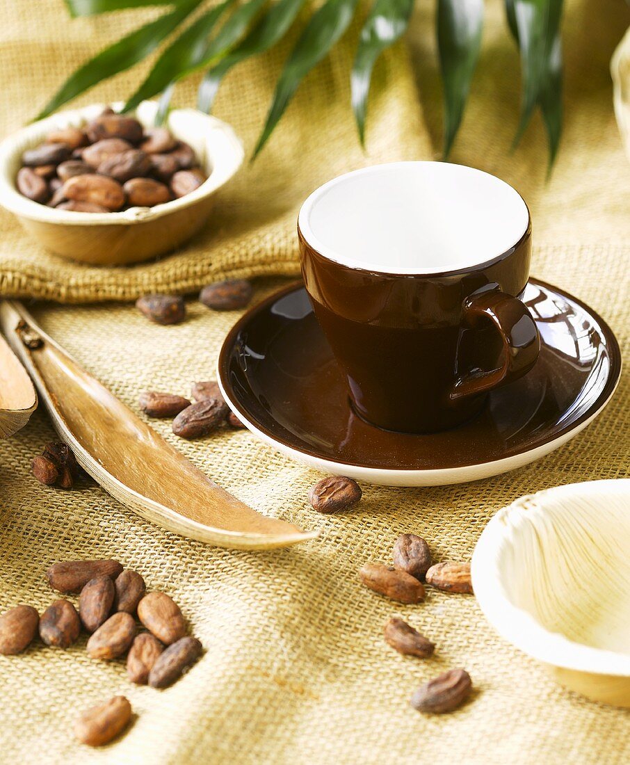 Braune Tasse auf Jutedecke mit Kakaobohnen und Palmenblatt