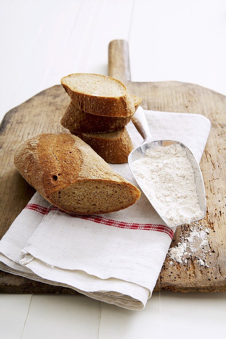 Wholemeal baguette, a piece and slices, flour in scoop