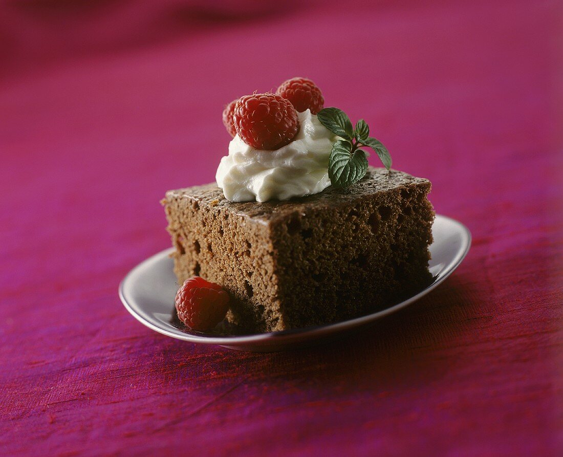 A piece of chocolate cake with cream and raspberries