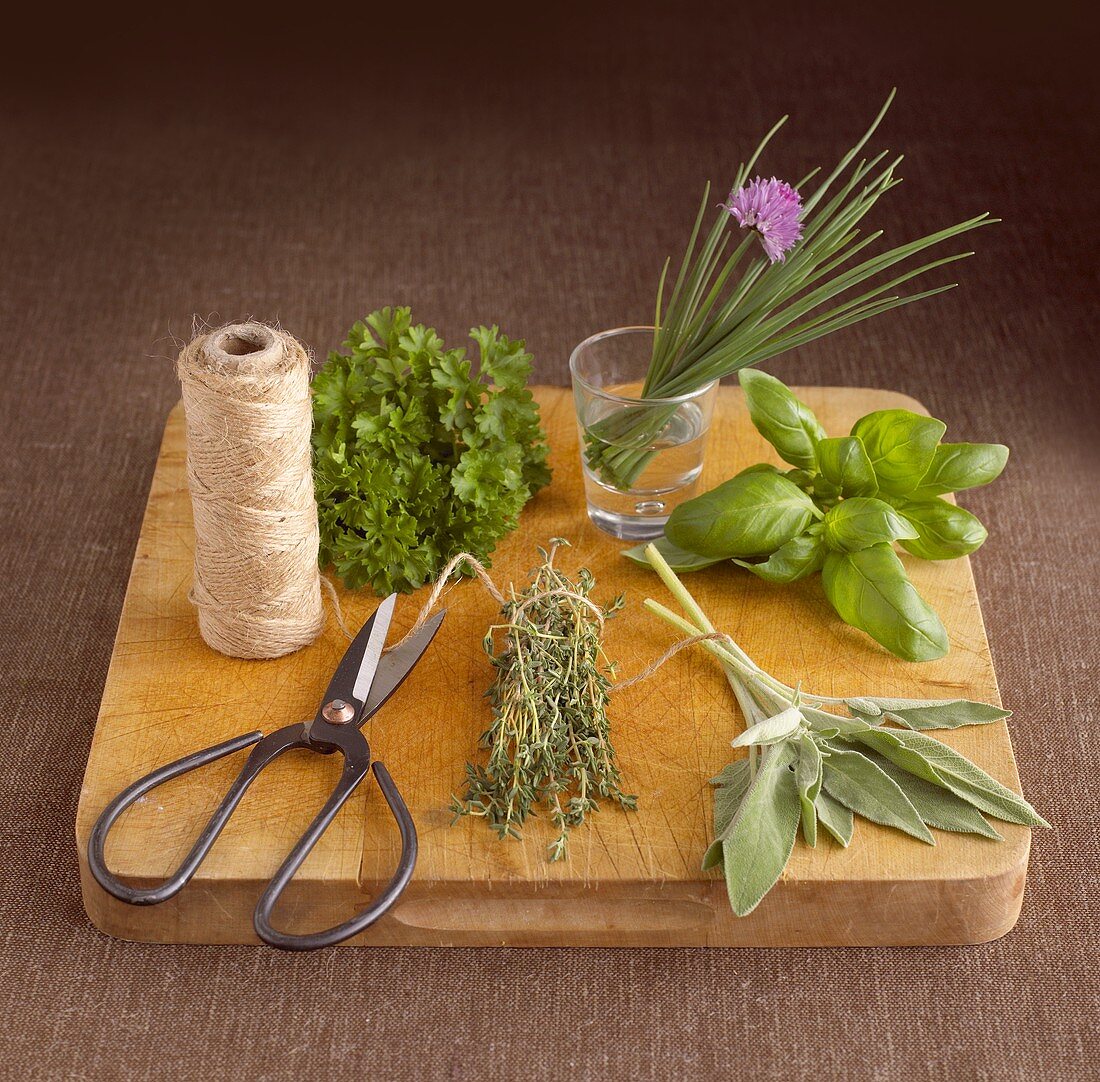 Fresh herbs, scissors and kitchen string on wooden board