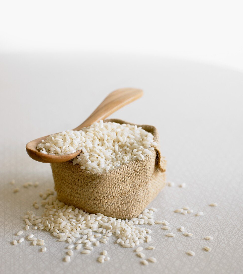 Arborio rice (risotto rice) on wooden spoon & in small sack
