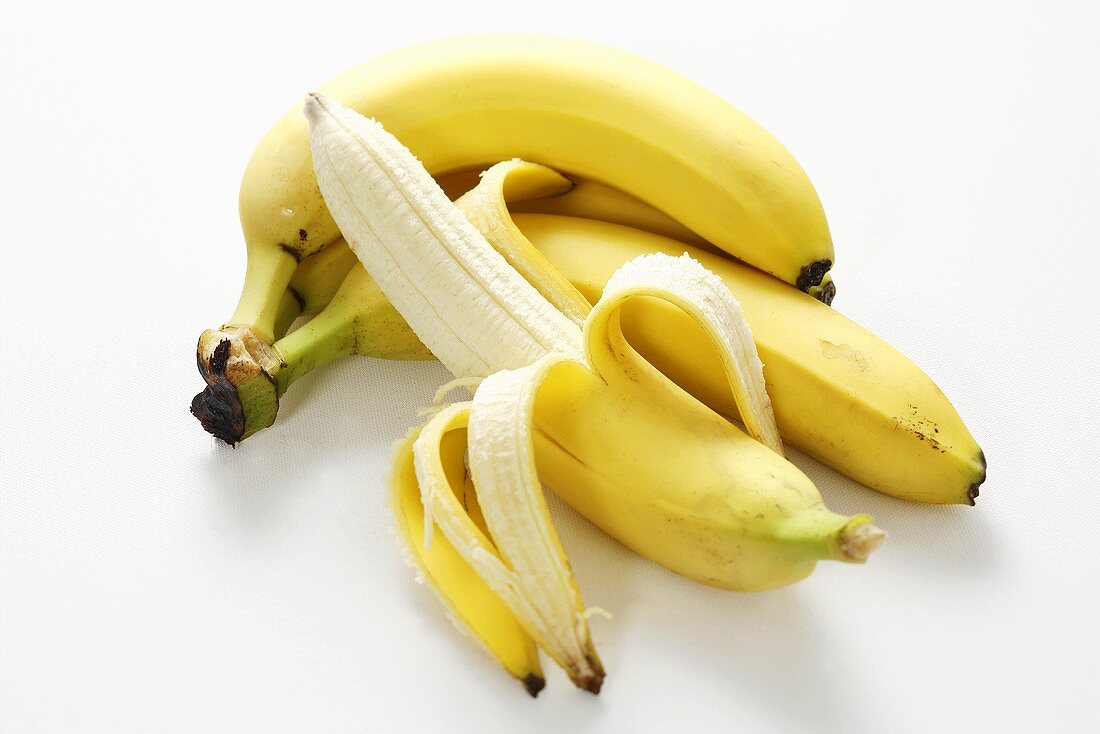 Halb geschälte Banane vor kleiner Bananenstaude