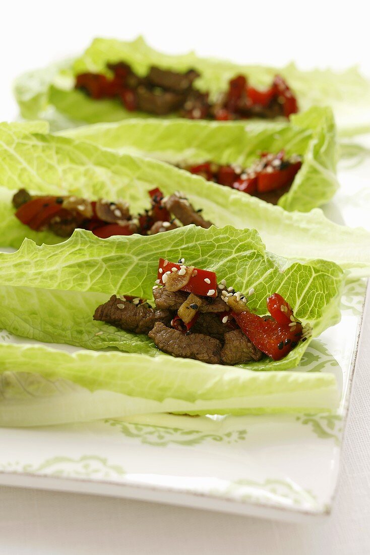 Beef with sesame seeds, ginger & peppers on lettuce leaves