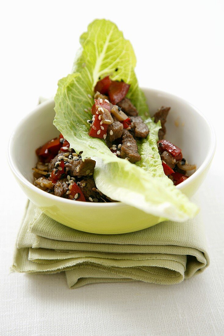 Beef with sesame seeds, ginger and peppers on lettuce leaf