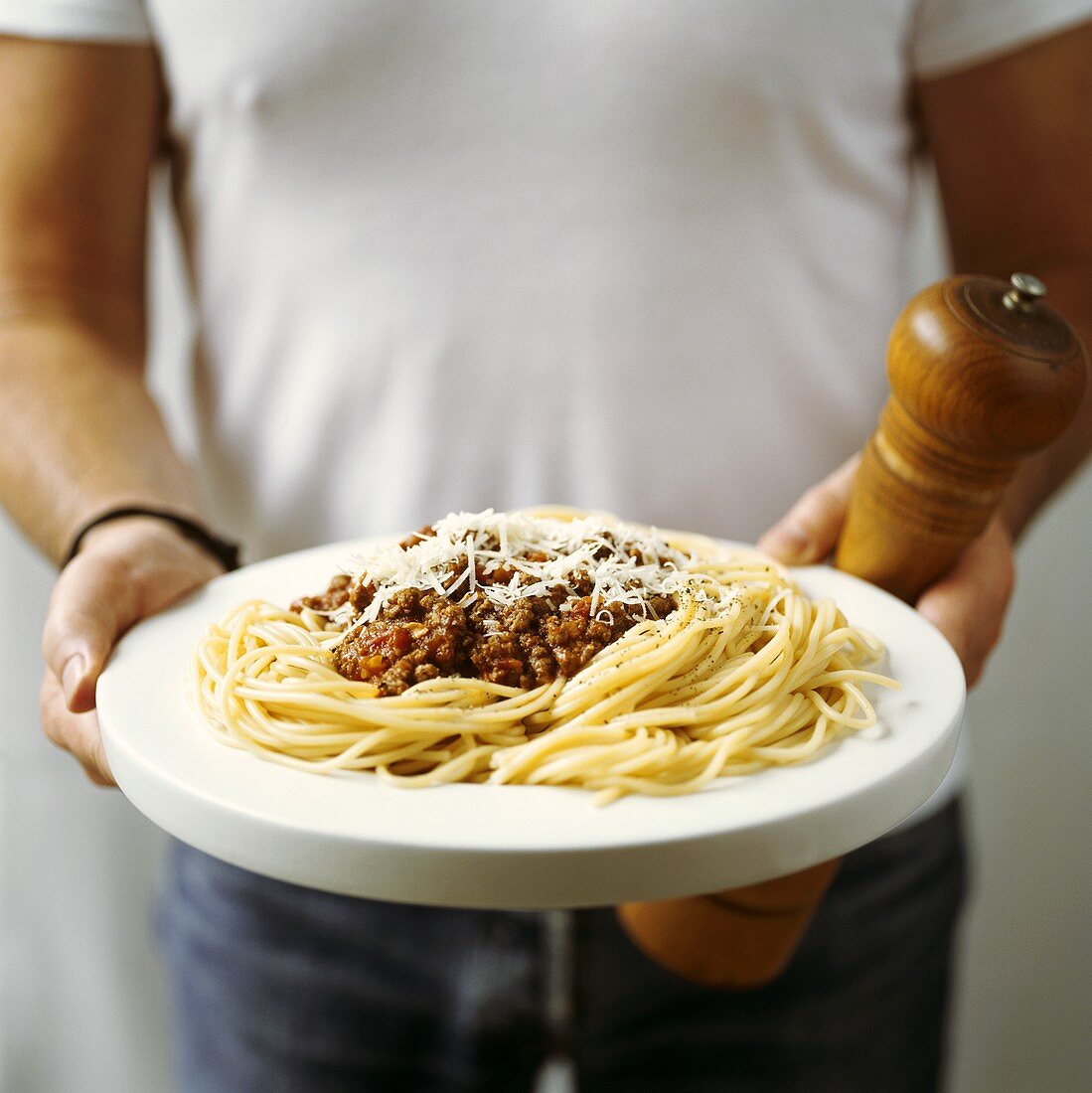 Man holding plate of spaghetti bolognese and pepper mill