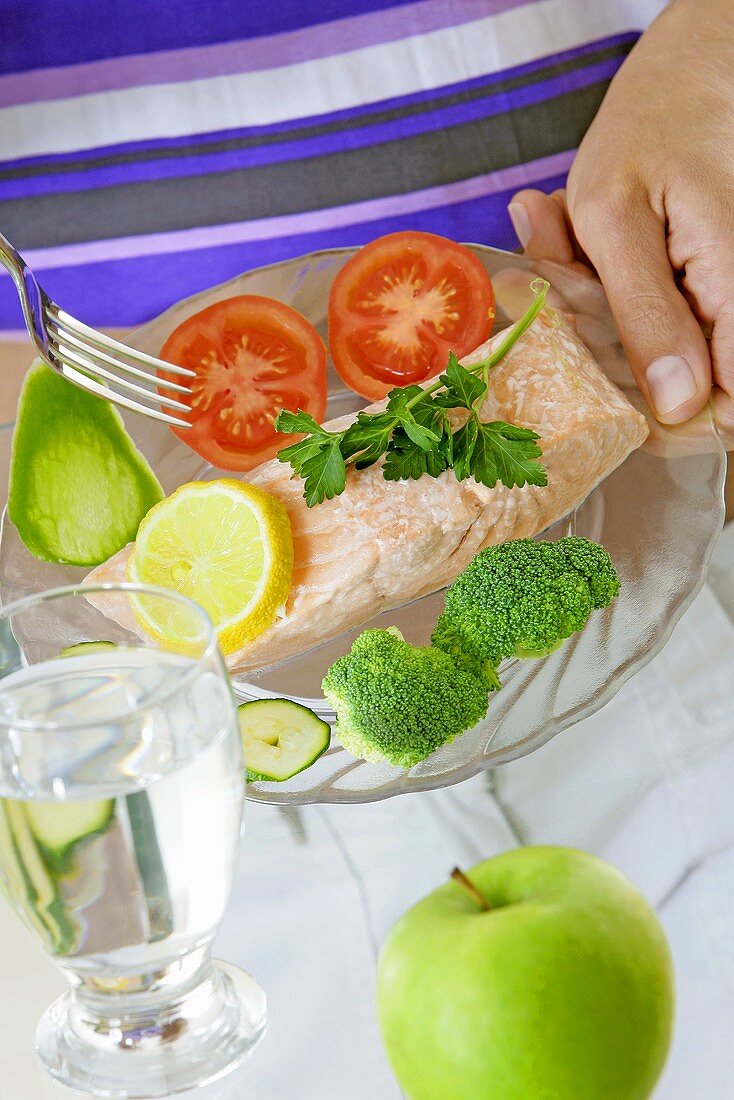 Lachsfilet mit Gemüse, ein Glas Wasser und ein Apfel