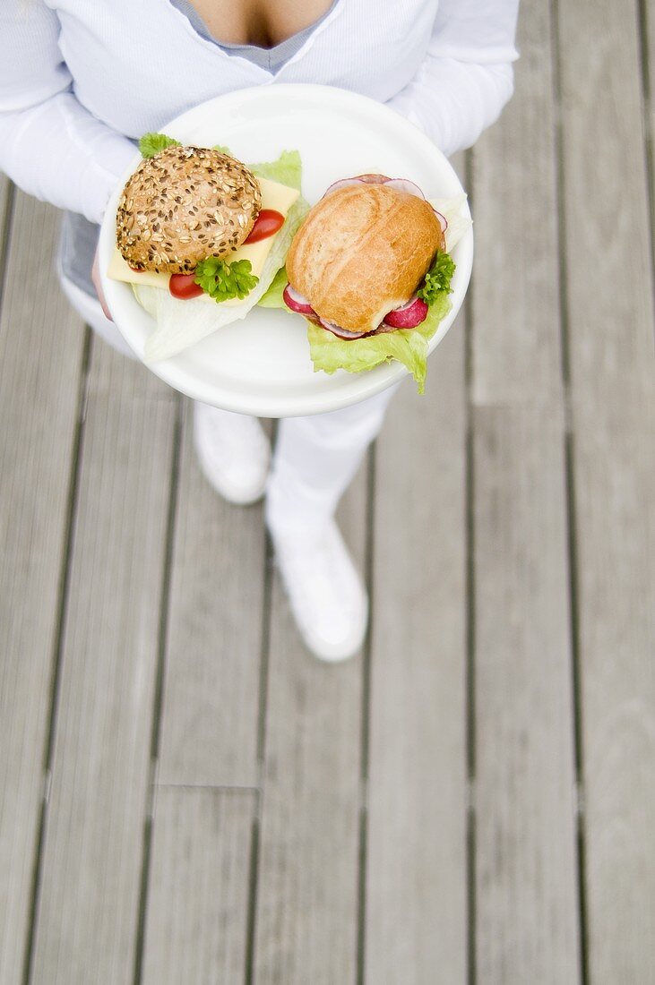 Junge Frau hält Teller mit zwei belegten Brötchen