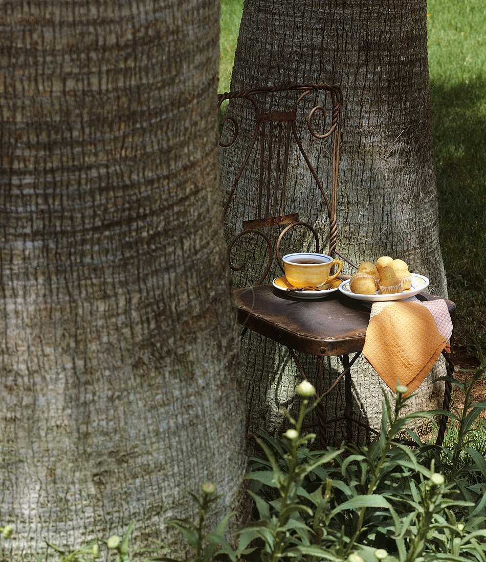 Stuhl mit Tee und Gebäck am Baumstamm