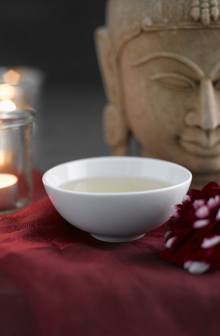 Grüner Tee in Teeschale, im Hintergrund Buddha-Kopf