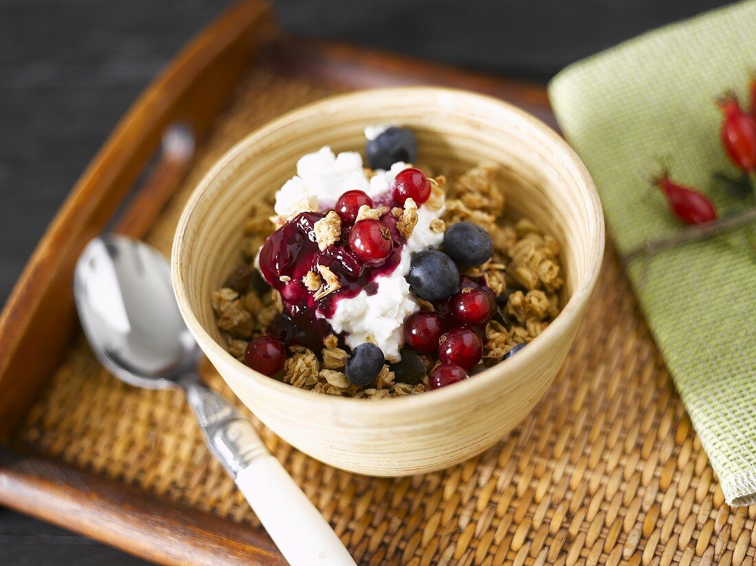 Müsli mit Joghurt und Beeren in Holzschale auf Holztablett