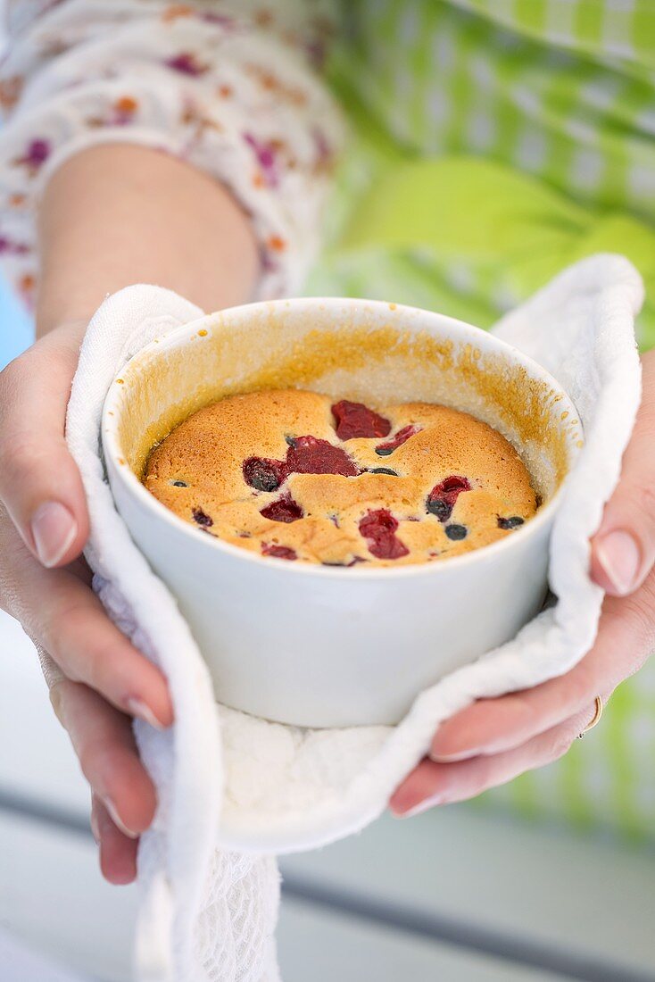 Hands holding a berry pudding in a baking dish