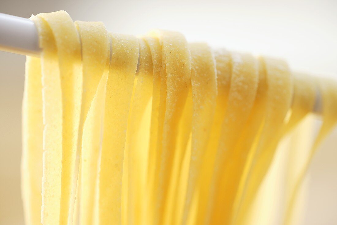 Home-made ribbon pasta hanging over kitchen spoon (close-up)