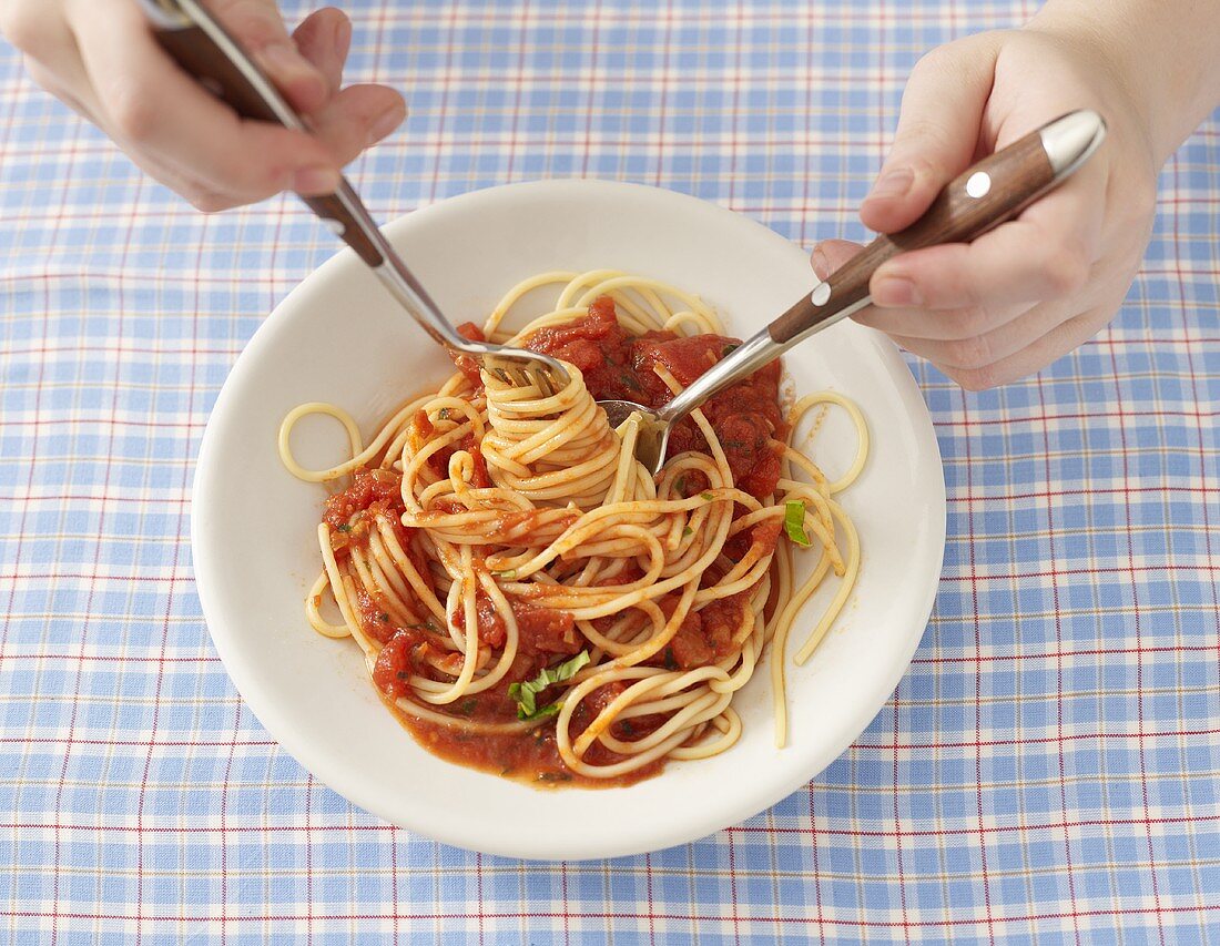 Spaghetti mit Tomatensauce mit Gabel und Löffel essen