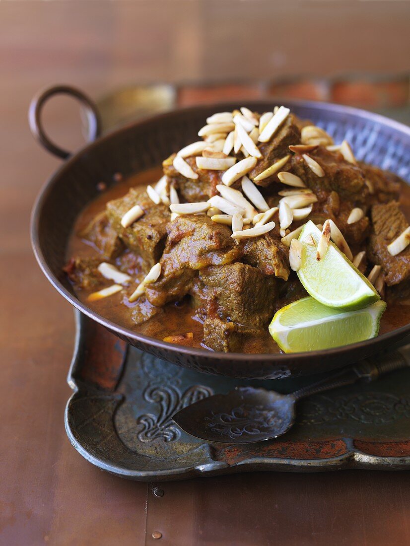 Beef curry with slivered almonds and lime wedges