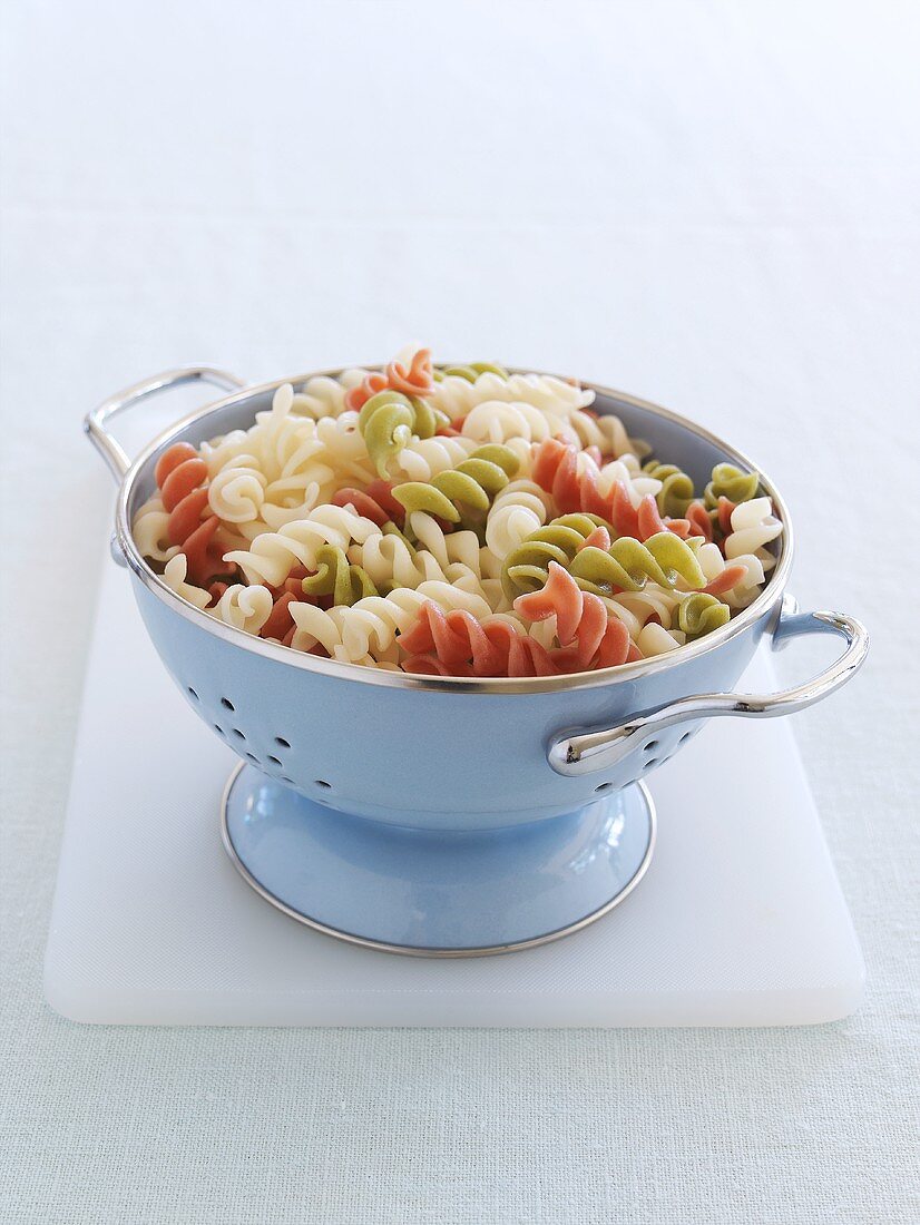 Cooked coloured spiral pasta in a metal colander