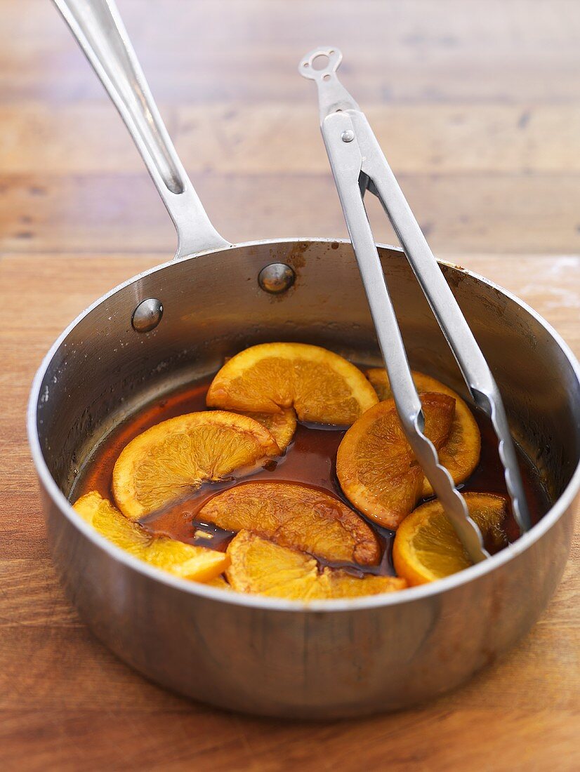 Caramelised orange slices in pan with tongs